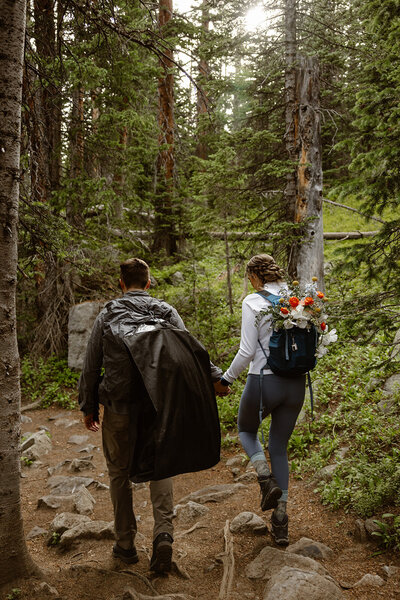 a bride and groom hike with wedding attire to colorado elopement in the mountains