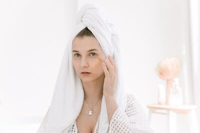women with a towl on her head putting on face cream