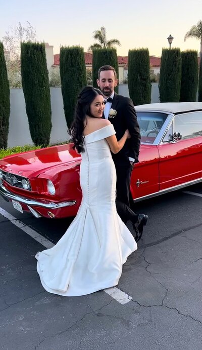 bride and groom embrace in front of classic red car