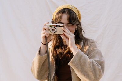 Photographer Hannah Kate holding camera, smiling in studio