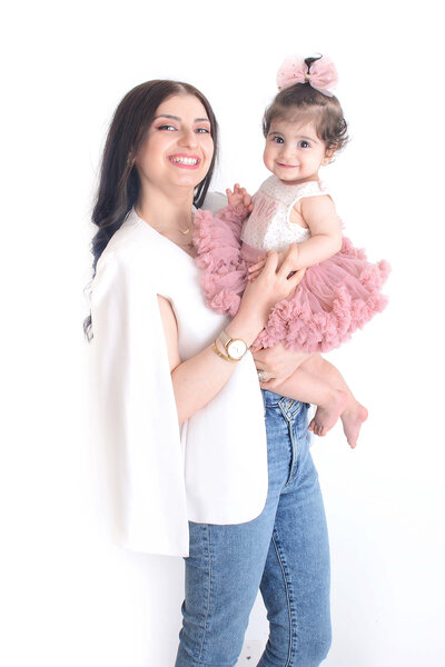 a mom smiles at the camera while holding her baby girl at their family phtooshoot