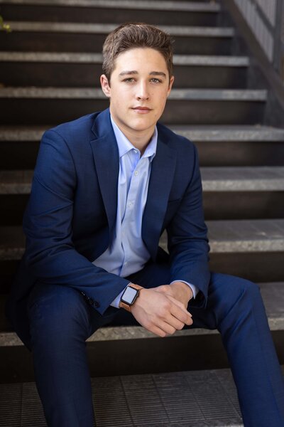 senior boy sitting on the steps in a blue suit