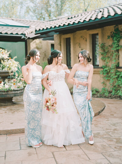 bridesmaids in dusty blue dresses helping bride get into dress for a cute getting ready photo on the balcony of a house in colorado