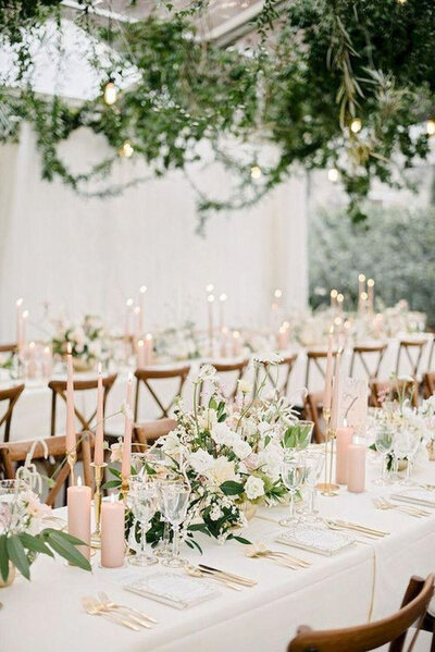 Long banquet table decorated with floral arrangements, candles, and greenery overhead
