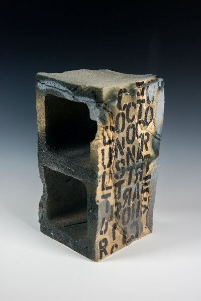 A cinder block that was hand made out of clay is decorated with underglaze to resemble graffiti and various other imagery