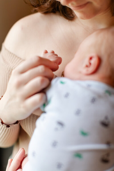 A mother and newborn son, son is resting on mothers chest while mother is holding his hand.
