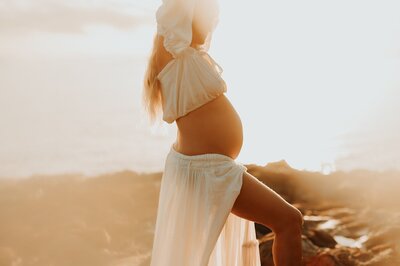 Profile image of a woman's pregnant belly as she poses for a  maternity session at sunset.