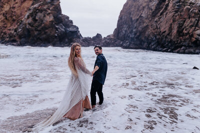 Destination elopement photographer captures couple walking into ocean during Big Sur Elopement