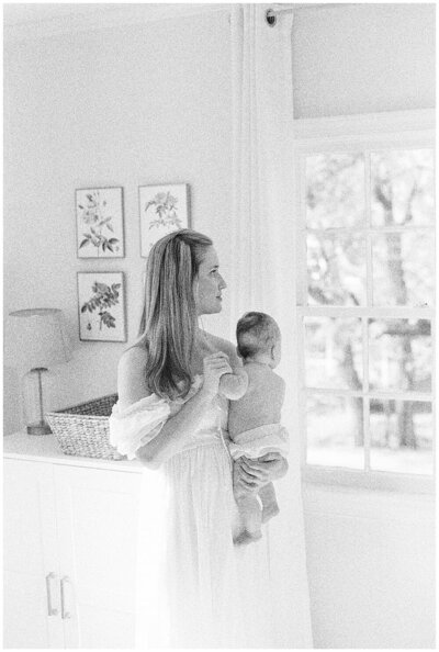 Marie Elizabeth Photographer, a newborn photographer in the DMV , holds her infant daughter and looks out the window.