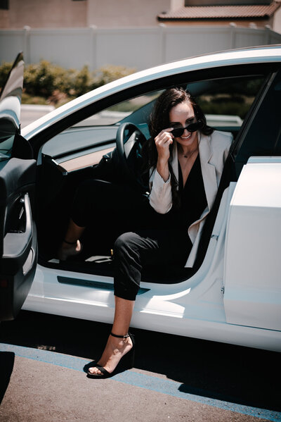 Bold lifestyle brand photo of a woman stepping out of her Tesla while removing sunglasses, conveying modern success