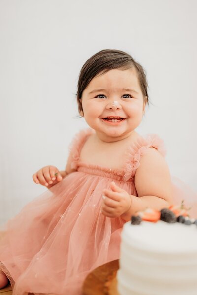 one year old looking at camera during first birthday photos. he wears a tie and sits in a basket