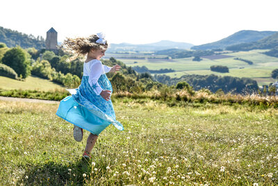 Young girl in Elsa dress running in a field with a castle behind her by Allison Burton