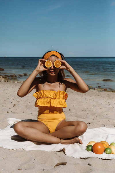 Woman holding up orange to her eyes, wearing an orange bikini