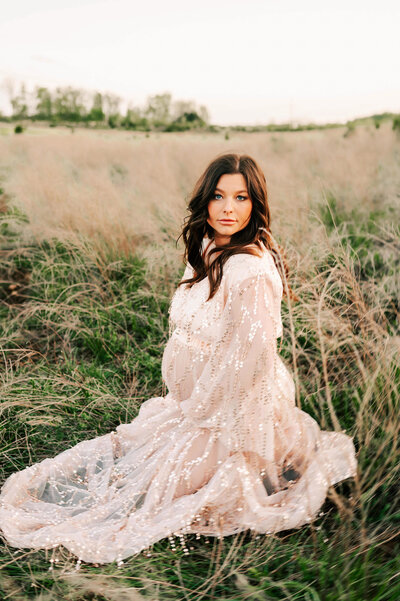 pregnant mom kneeling in field captured by Branson MO motherhood and family photographer