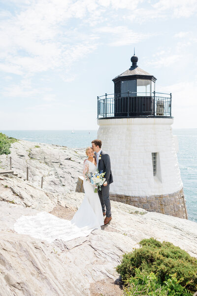 Groom kissing his bride on the forehead in front of a lighthouse on the water in Newport, RI