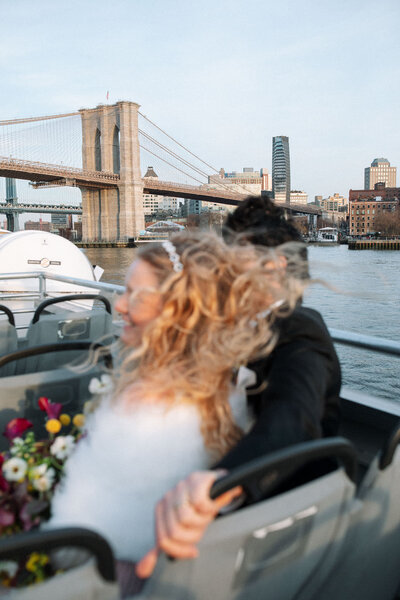 NYC city hall elopement couple on nyc ferry with brooklyn bridge in the background and hair flying in wind