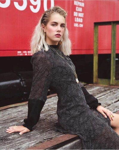 A girl sitting in front of a train wearing a black dress