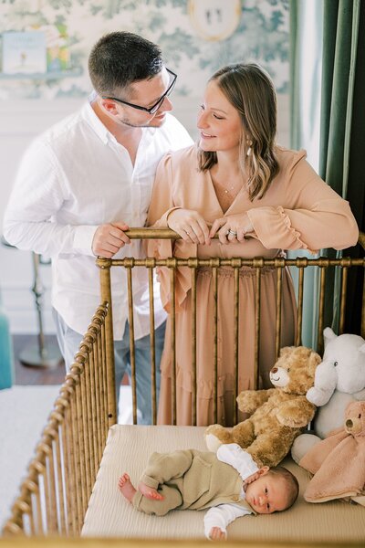 Mother and father stand in their sons high end nursery with a gold crib during their newborn session with Philadelphia photographer Samantha Jay