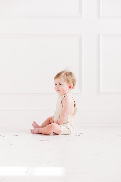 A baby happily sitting on the floor in a white room captured by a Charlotte NC baby photographer.