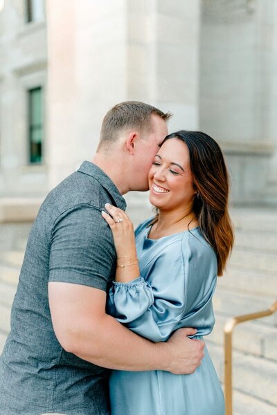 Engaged couple sharing a joyful moment, with the groom whispering in his fiancée's ear while she smiles brightly