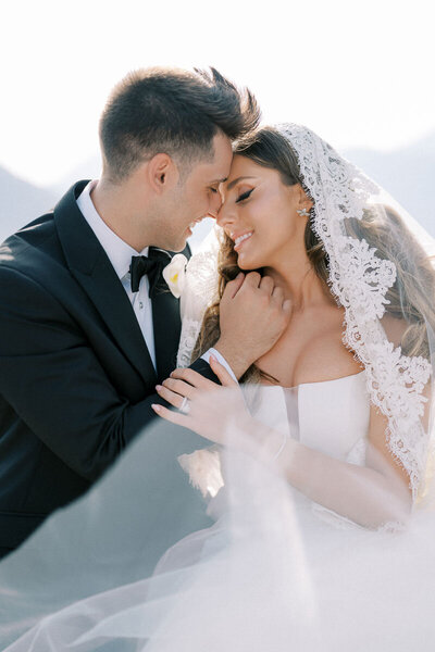 Romantic close-up of bride and groom touching foreheads with lace veil blowing in soft light, captured near Toronto