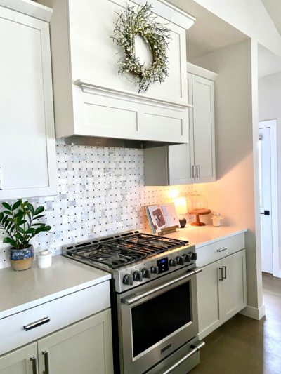 Modern white kitchen with stainless steel stove, subway tile backsplash, and a decorative wreath above the range hood.