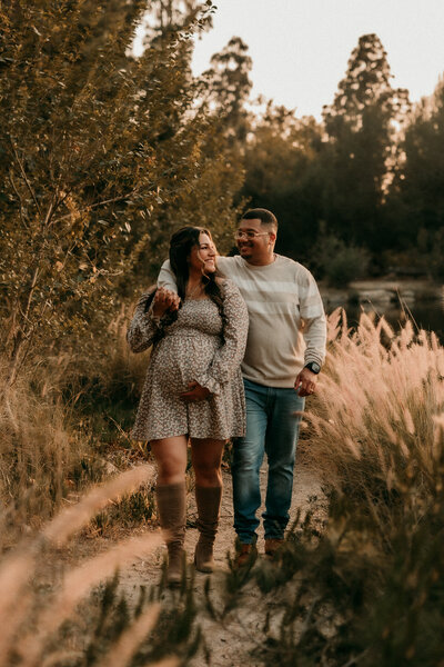 Pregnant couple walking through tall grass during a golden hour maternity session at Yorba Regional Park in Yorba Linda