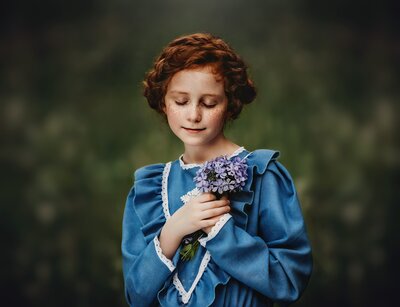 Young girl with red hair in a braided crown in a blue dress in a field