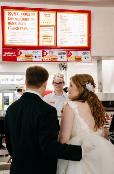 Bride and groom facing each other ordering in a fast food