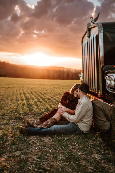 Couple snuggling up leaning onto a semi at sunset. 