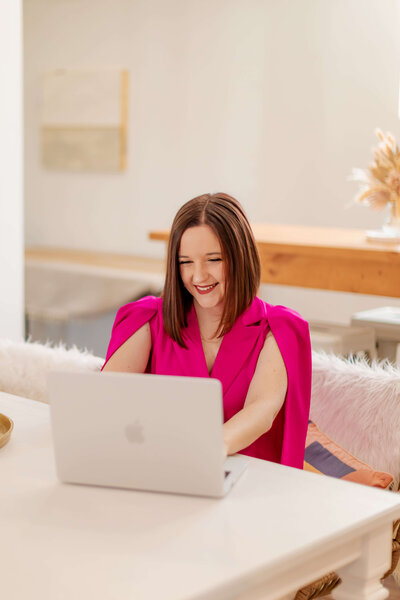 Woman wearing bright pink blazer and typing on laptop