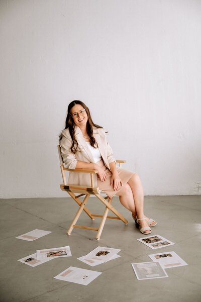 lubbock newborn photographer sitting in chair legs crossed over leaning on one hand on arm of chair with maternity style guide papers randomly scattered on floor