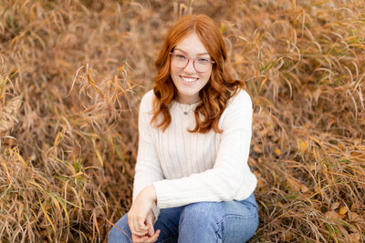 Senior representative sits in a field of grass while smiling.