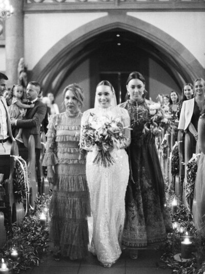 Bride walks down the aisle with wedding bouquet and two attendants during wedding ceremony in church