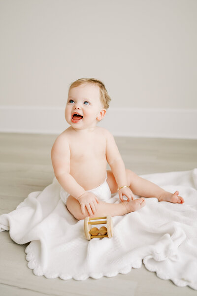 1 year old baby girl in white diaper cover plays in Raleigh photography studio during simple baby session by Worth Capturing
