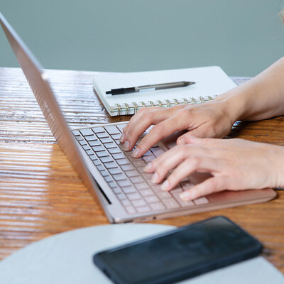 Hands typing on keyboard at desk with cellphone and notepad