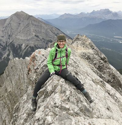 A female hiker seating on a mountain peak, wearing the Terminator knee brace from Lethbridge Orthotics.