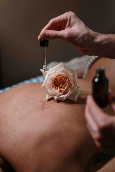 A drop of rose-infused essential oil being applied to the back, creating a luxurious and calming aromatherapy massage experience.