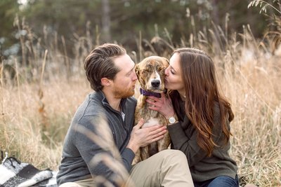 Engaged couple kiss their dog's cheeks as they pose for an engagement photo session.