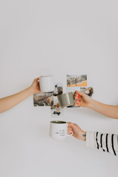 Hands holding up mugs in front of a collage wall
