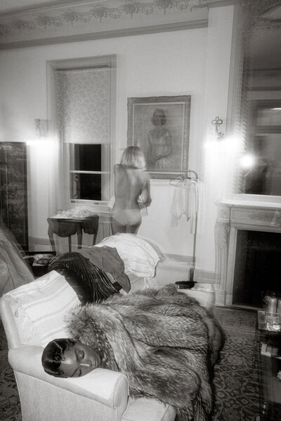 Black and white photo of a bride changing into her dancing dress while her friend is sleeping on the couch.
