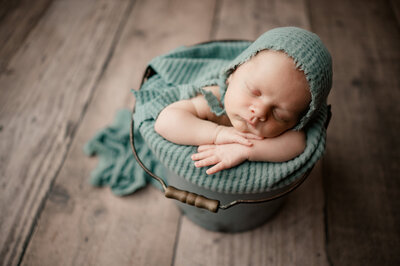 newborn in bucket with light green blankets