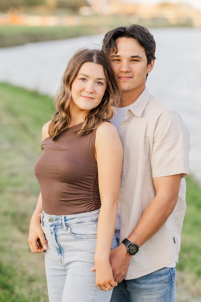 Engaged couple holding hands by the river in Fort Worth, Texas during golden hour, with soft natural lighting and relaxed outfits perfect for a casual engagement session.