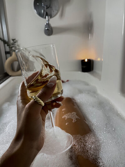 Woman sitting in a bathtub holding up a wine glass