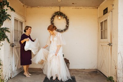 Bride holding dress while mom helps her put her wedding dress wrap on