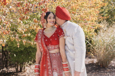 South Asian couple poses in front of fall foliage in their traditional wedding garb.