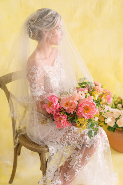 A bride with her veil on, sitting on a rustic chair staring into the distance while holding a beautiful bouquet of pink flowers found inside of The Doyle in Las Vegas, Nevada.