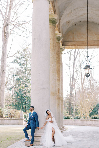 bride and groom holding hands lightly as they lean against a column on the Swan House