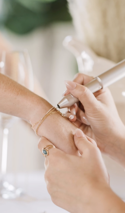 Permanent bracelet welding in progress on wrist with gold chains.