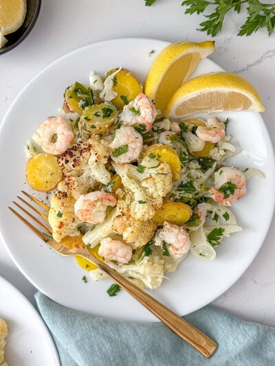 A plate of sautéed shrimp with cauliflower and carrots, garnished with parsley and lemon wedges.